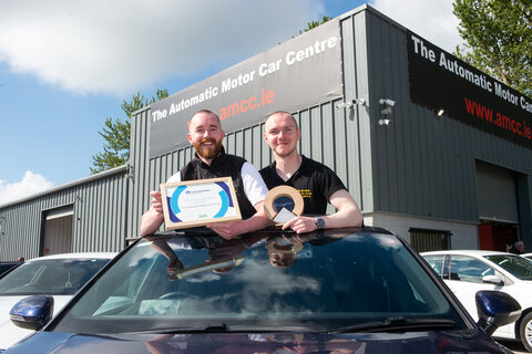 Two men coming out of the top of the car holding a certificate and trophy