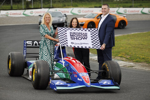 two close brothers motor finance meployess posing with a female f1 racer with the flag that says European motor show and close brothers motor finance 
